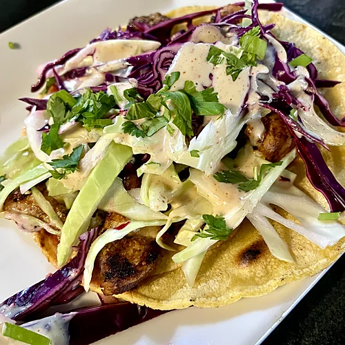 Corn tortilla tacos topped with red and green cabbage slaw, cilantro and creamy sauce