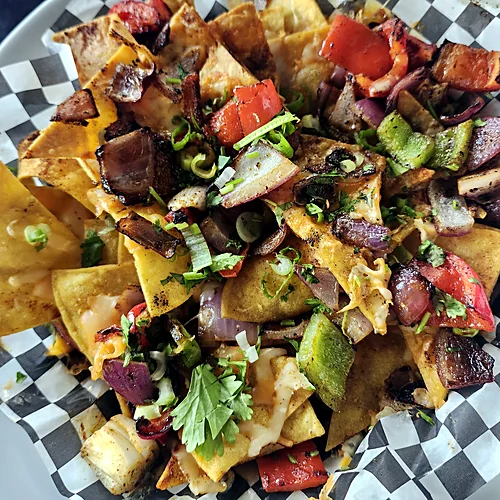 Loaded nachos with grilled peppers, onions, steak and melted cheese in a checkered paper-lined basket
