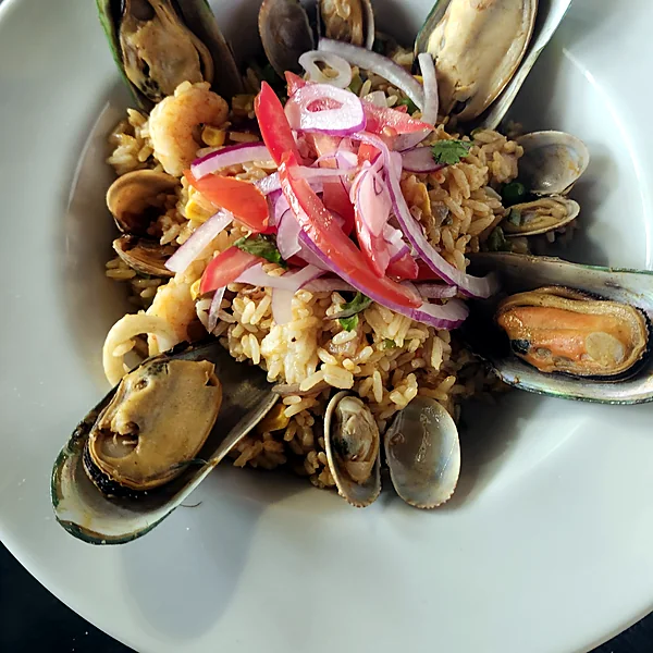 Seafood rice with mussels, clams, shrimp, tomato and red onion in a white bowl