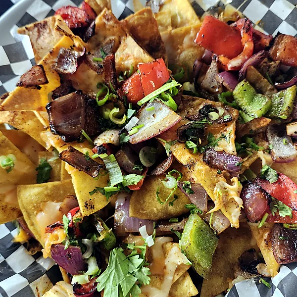 Loaded nachos with grilled peppers, onions, steak and melted cheese in a checkered paper-lined basket
