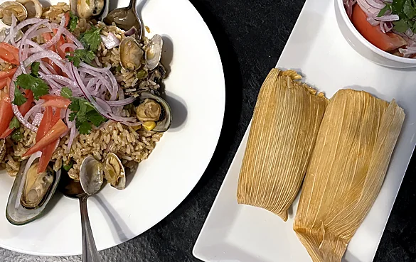 Seafood rice with mussels and clams beside two humitas in corn husks and a tomato onion salad