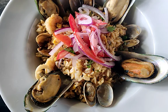 Seafood rice with mussels, clams, shrimp, tomato and red onion in a white bowl
